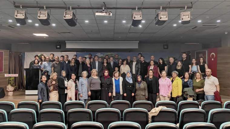Bir grup insan, bir etkinlikte sahne önünde topluca poz veriyor.
