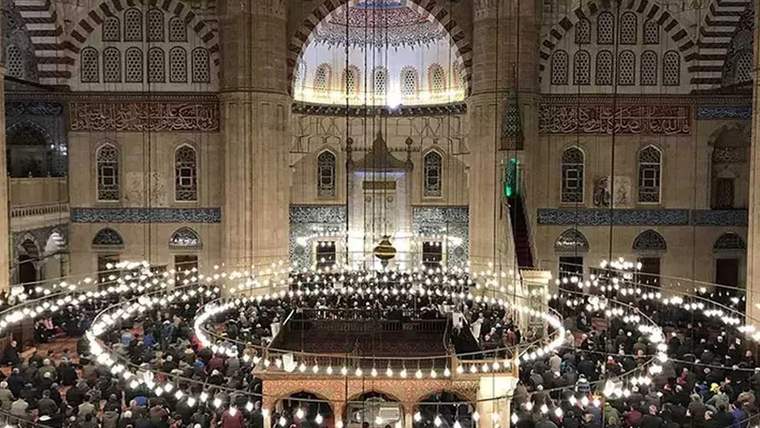 Bir cami içinde, cemaatin toplandığı ve avizelerin asılı olduğu bir görüntü.