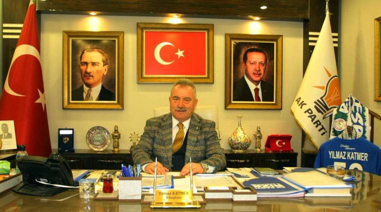Bir masa başında oturan bir kişi, arkasında Türk bayrağı ve iki portre var.
