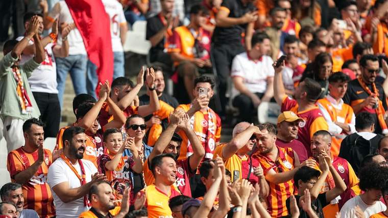 Tribünde sarı-kırmızı formalar ve atkılar taşıyan taraftarlar, ellerini kaldırarak tezahürat yapıyor.