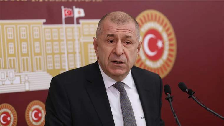 Kırmızı arka planda Türkiye bayrağı ve TBMM simgeleriyle bir kişi konuşma yapıyor.