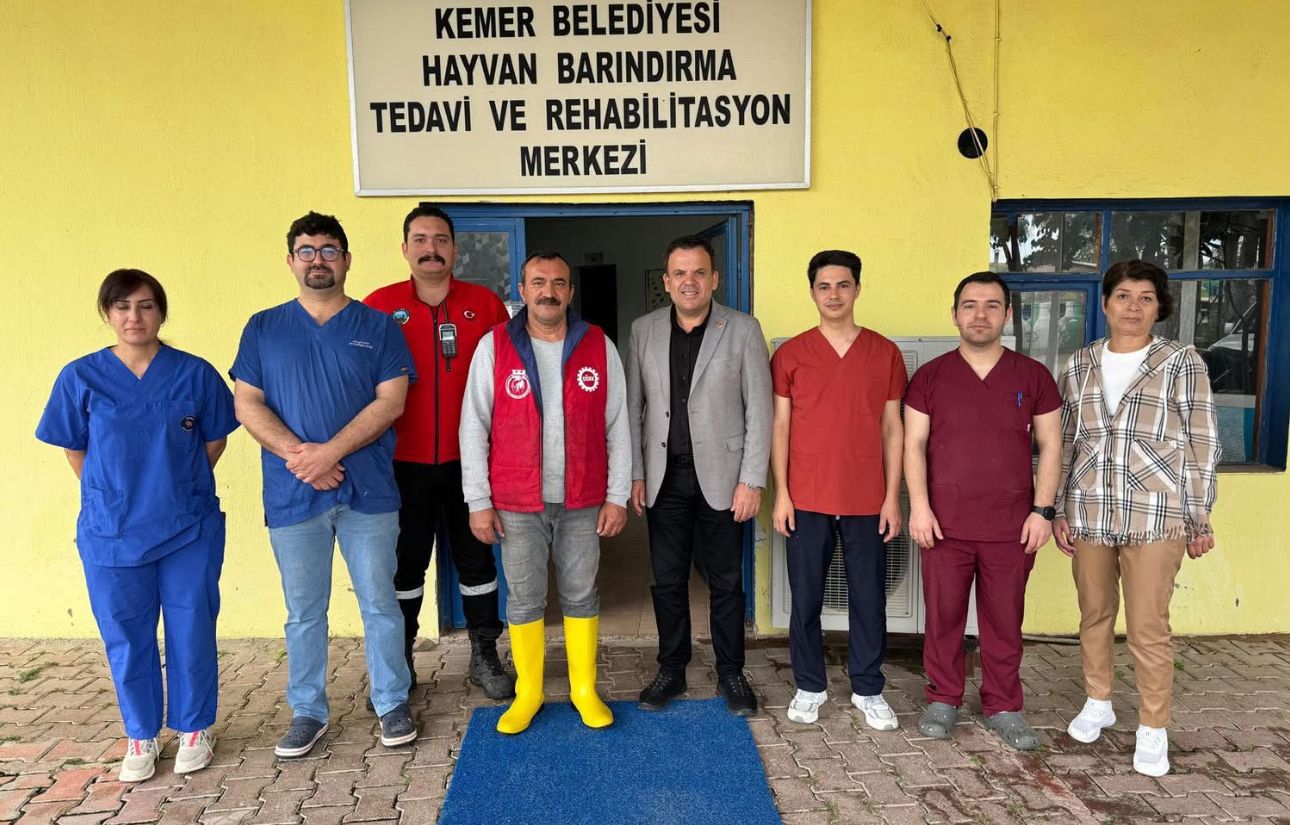 “Kemer Belediyesi Hayvan Barındırma Tedavi ve Rehabilitasyon Merkezi” tabelası önünde sekiz kişi duruyor.