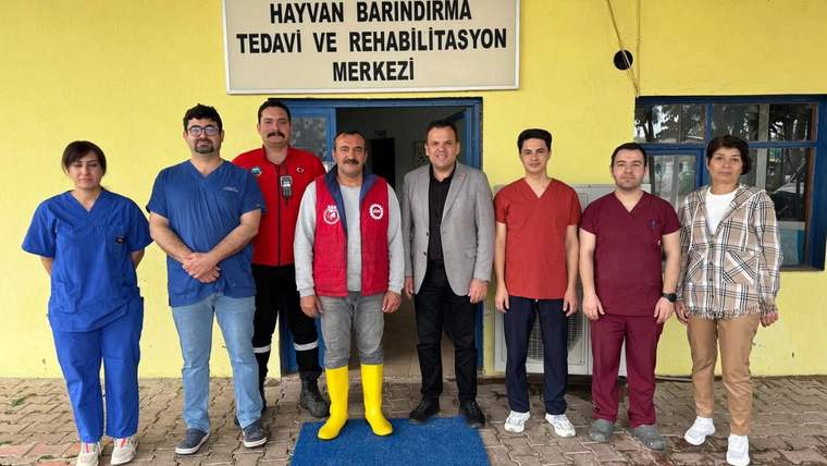 “Kemer Belediyesi Hayvan Barındırma Tedavi ve Rehabilitasyon Merkezi” tabelası önünde sekiz kişi duruyor.
