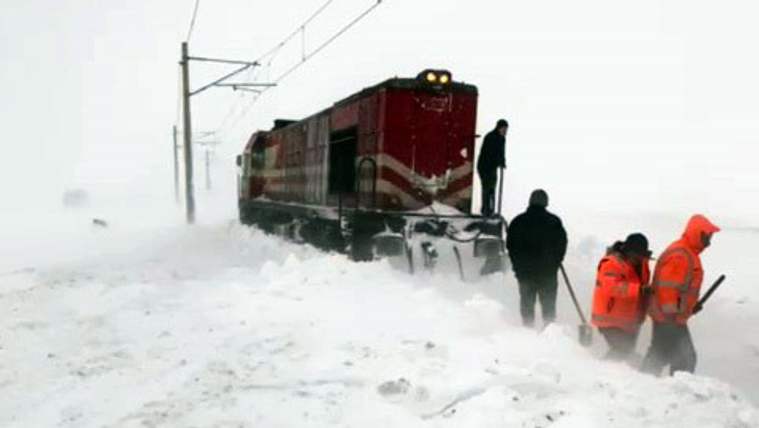Karla kaplı raylarda bir tren ve etrafında çalışan işçiler, kar temizliyorlar.