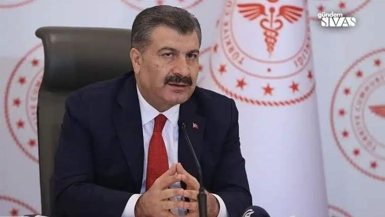 Kırmızı kravat takan bir kişi, masada ellerini birleştirerek konuşuyor.