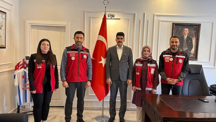 Türk bayrağının önünde, sosyal hizmetler çalışanları ve bir kişi poz veriyor.