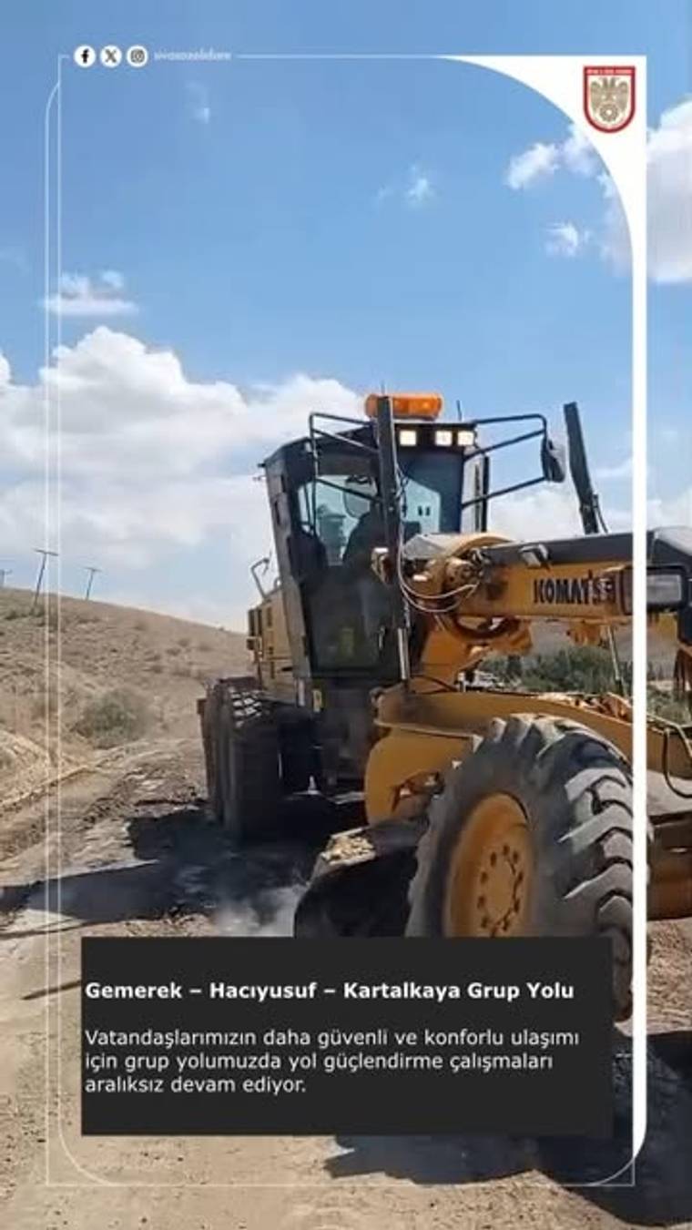 KOMATSU marka greyder, toprak yolda çalışırken yanında kurak ve engebeli arazi görülüyor.