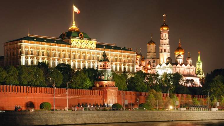 Gece ışıklandırılmış Kremlin kompleksi, kırmızı surları ve nehir kıyısındaki yansımalarıyla görülüyor.