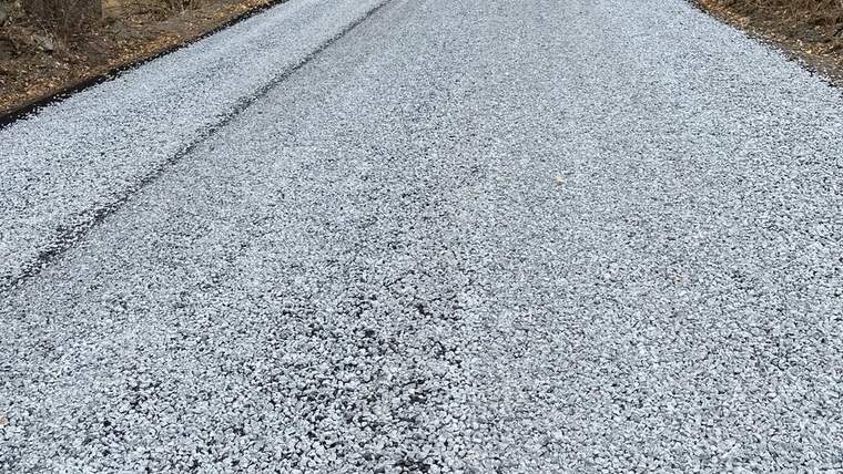 Yeni asfalt kaplama ile düz bir yol görünümü, yol kenarında ağaçlar yer alıyor.