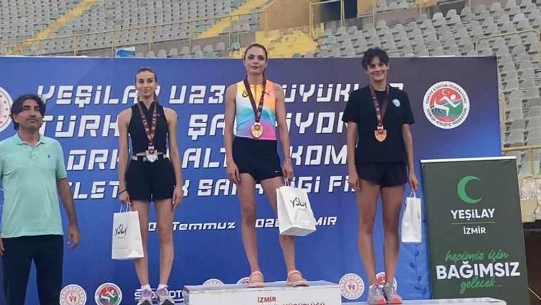 Üç kadın sporcu, madalyaları ve ödül torbalarıyla podyumda duruyor; arkada spor salonu tribünleri görülüyor.