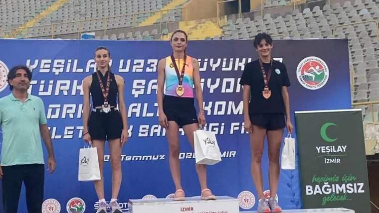 Üç kadın sporcu, madalyaları ve ödül torbalarıyla podyumda duruyor; arkada spor salonu tribünleri görülüyor.