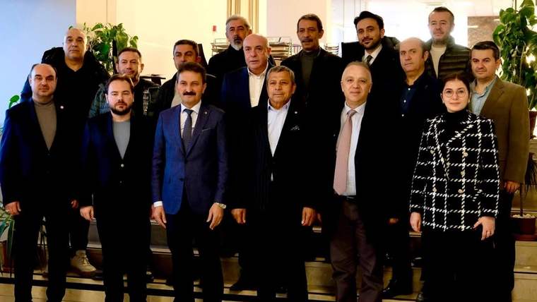 İç mekânda, takım elbiseli ve günlük giyimli kalabalık bir grup birlikte poz veriyor.