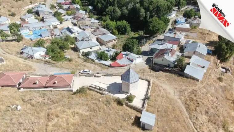 Küçük bir yerleşim alanında, etrafında evler bulunan bir türbe görünmektedir.