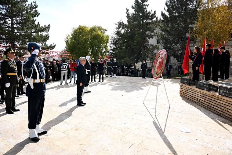 Açık alanda tören kıtasındaki üniformalı kişi selam dururken, kalabalık ve Türk bayrakları görülüyor.