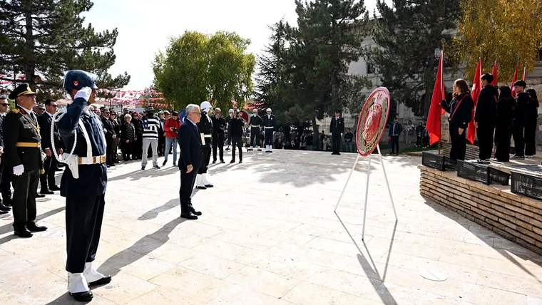 Açık alanda tören kıtasındaki üniformalı kişi selam dururken, kalabalık ve Türk bayrakları görülüyor.