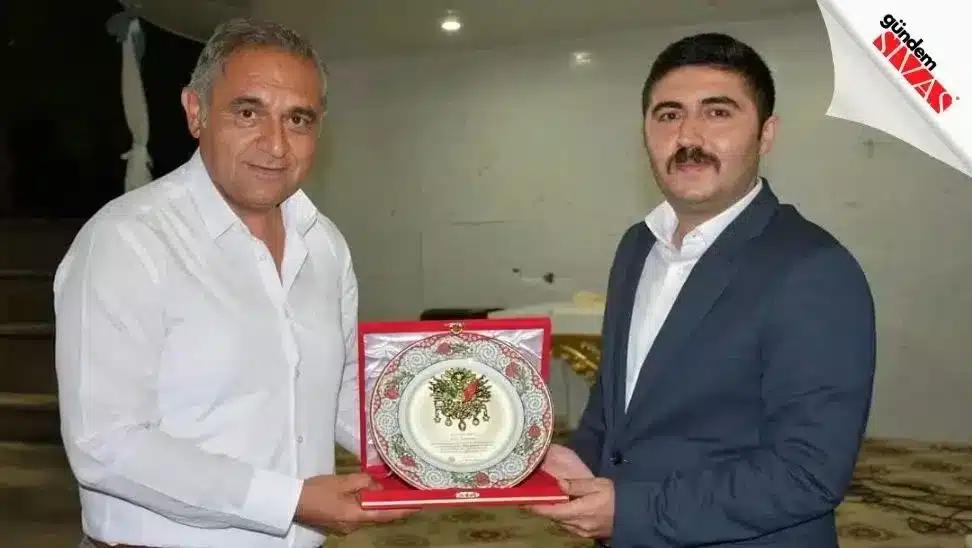 İki erkek, üzerinde çiçek desenleri bulunan dekoratif tabağı kırmızı kutusuyla birlikte tutuyor.