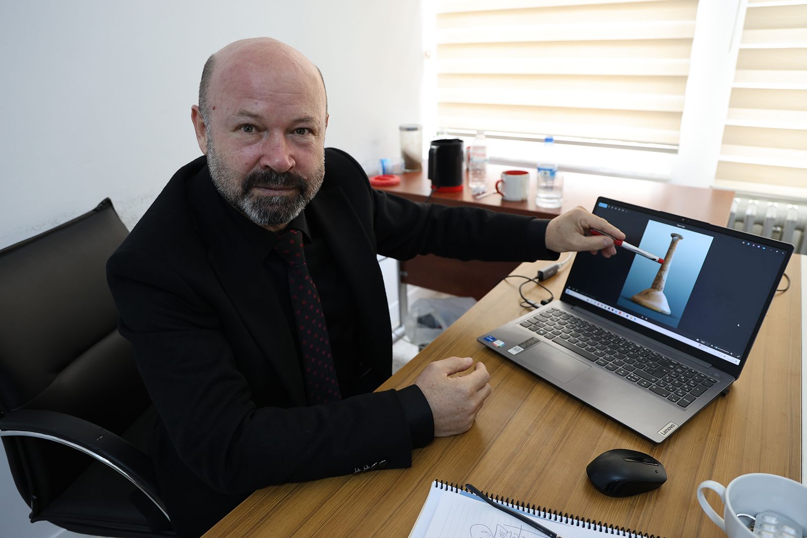 Bir kişi, bilgisayar ekranında antik bir şişe resmi gösteriyor.