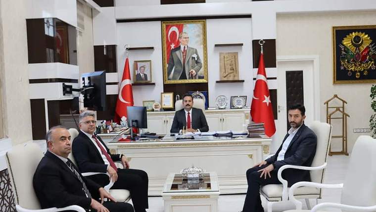 Makam odasında biri masanın arkasında, üçü karşısında oturan dört erkek ve iki Türk bayrağı görülüyor.