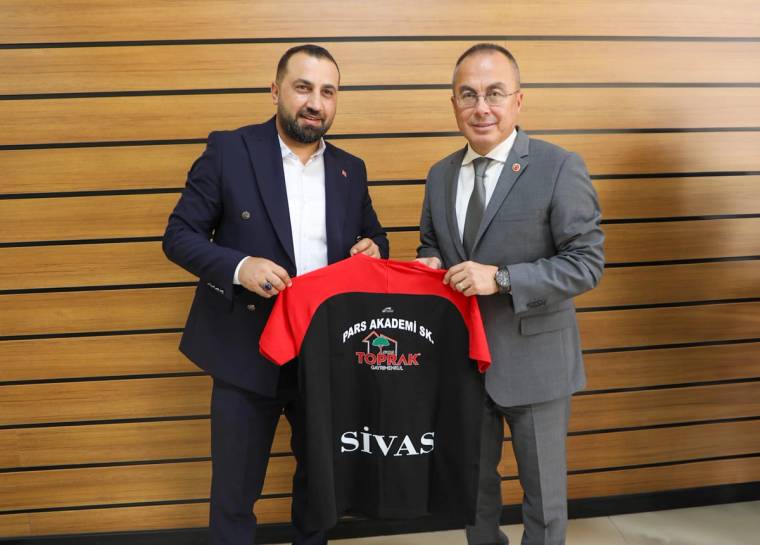 İki erkek, üzerinde Pars Akademi ve Sivas yazan siyah-kırmızı voleybol formasını birlikte tutuyor.