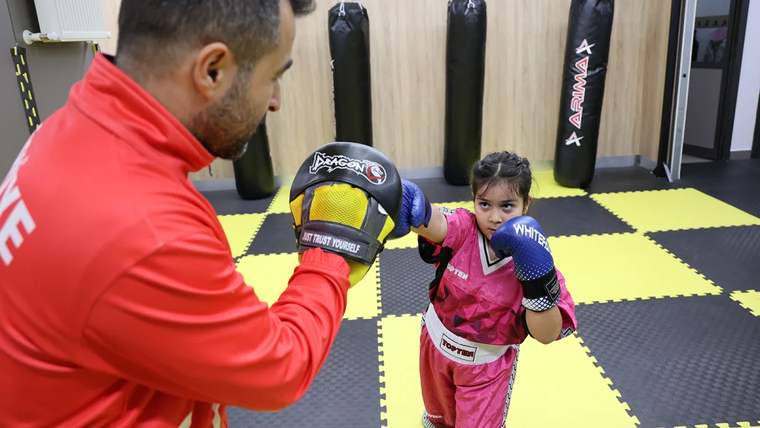 Antrenman yapan bir çocuk, antrenörüyle birlikte kick boks yapıyor.