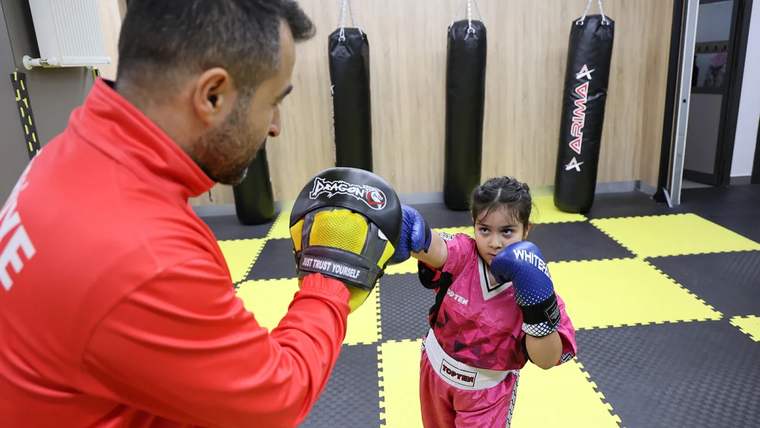 Antrenman yapan bir çocuk, antrenörüyle birlikte kick boks yapıyor.