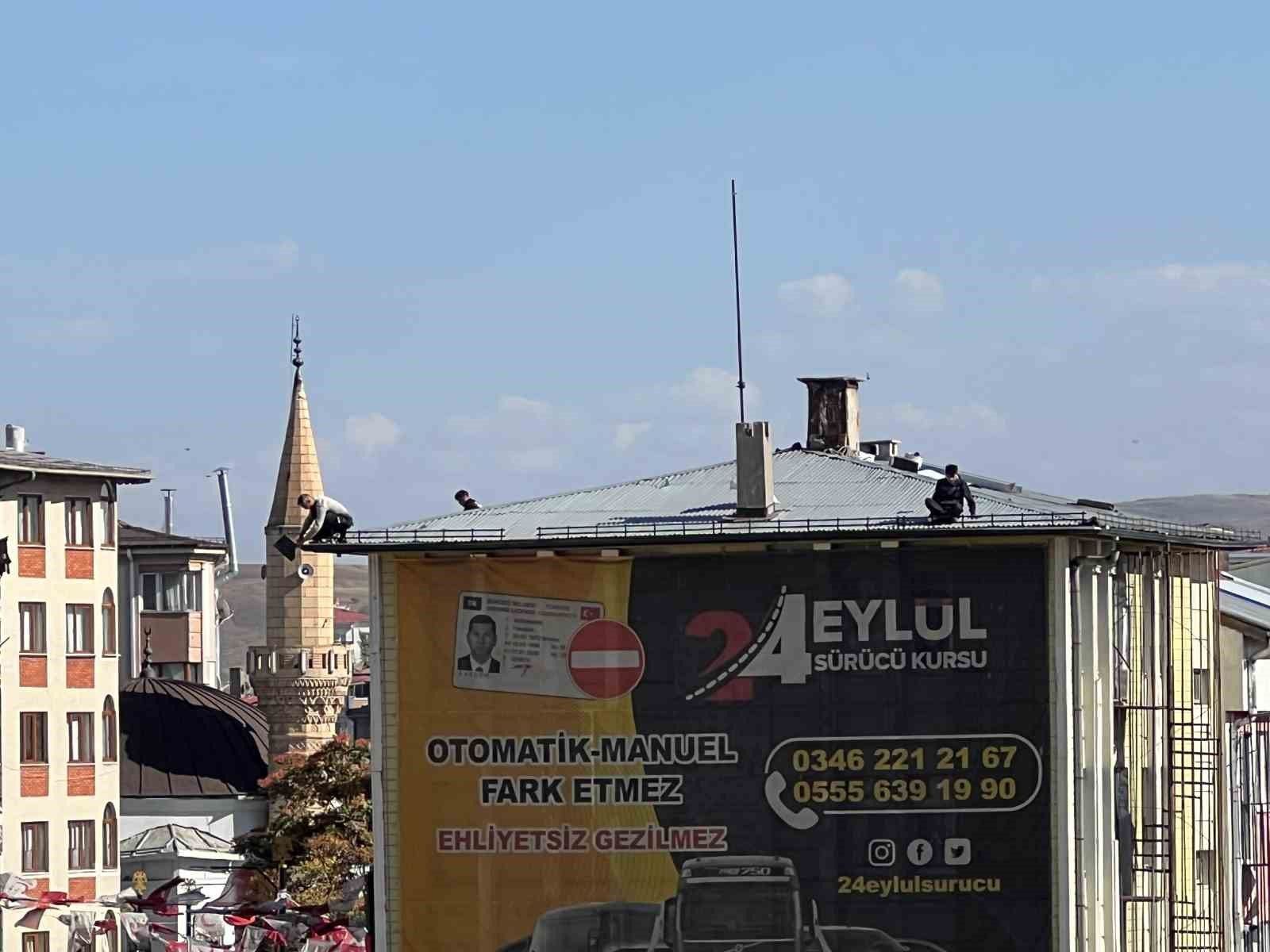 Sürücü kursu tabelasının bulunduğu binanın çatısında üç kişi, anten ve baca çevresinde görülüyor.