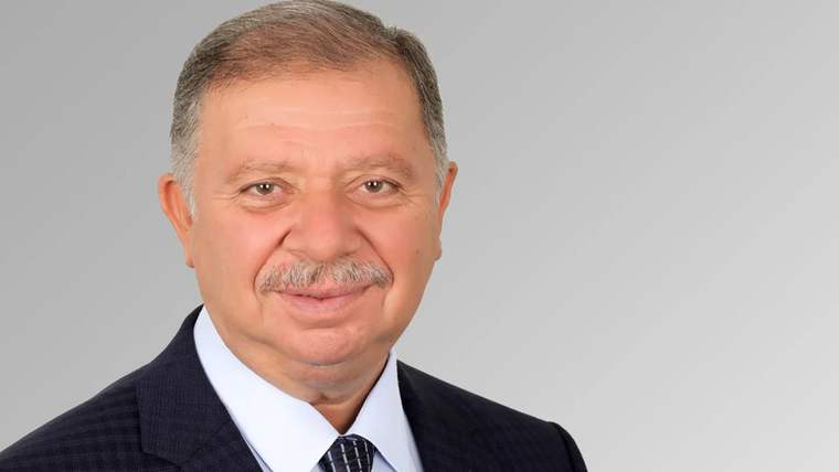 Gri arka planda, takım elbise giymiş bir adam gülümseyerek poz veriyor.