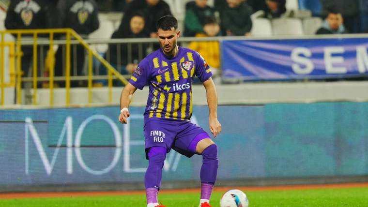 Sarı mor formasıyla bir futbolcu, topa doğru yönelmiş halde duruyor.