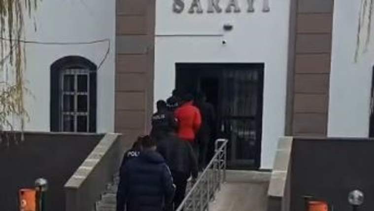 Polis eşliğinde iki kişi, üzerinde "ADLİYE SARAYI" yazan binanın merdivenlerinden çıkıyor.
