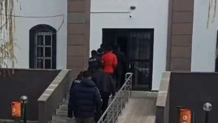 Polis eşliğinde iki kişi, üzerinde "ADLİYE SARAYI" yazan binanın merdivenlerinden çıkıyor.