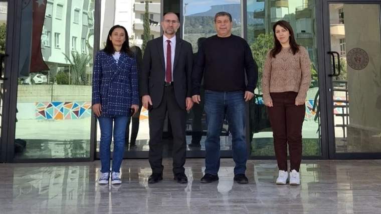 Cam kapılı bir binanın girişinde, iki kadın ve iki erkek yan yana ayakta duruyor.