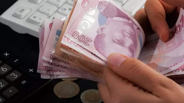 Bir kişinin elinde 200 TL banknotlar var, arka planda bir hesap makinesi ve klavye görünüyor.
