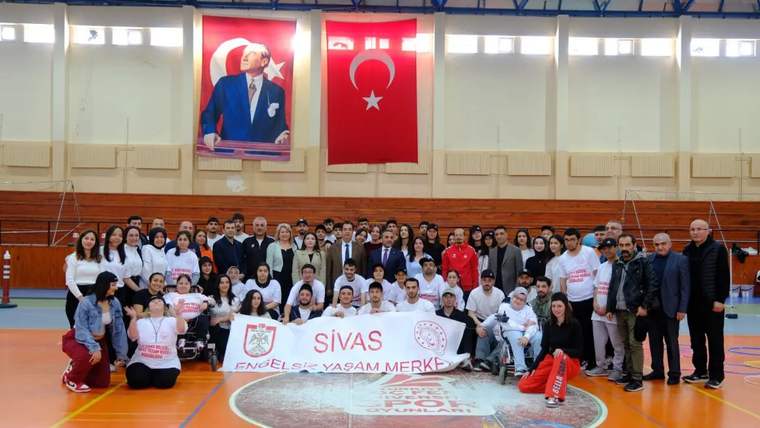 Spor salonunda, özel gereksinimli bireyler ve katılımcılar bir arada, büyük bir pankart tutuyor.