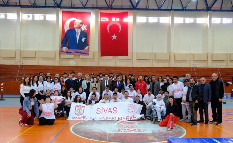 Spor salonunda, özel gereksinimli bireyler ve katılımcılar bir arada, büyük bir pankart tutuyor.