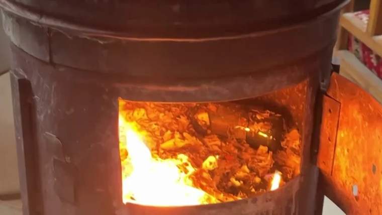 Ateşin yandığı bir sobanın iç kısmı, alevler ve yanmış odun parçaları görünüyor.
