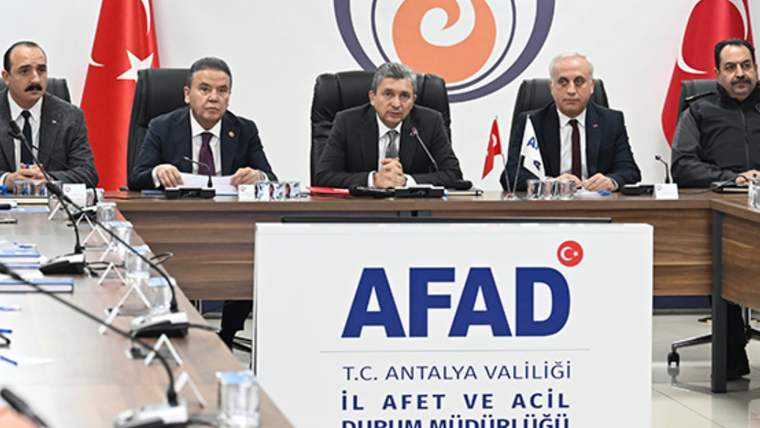Toplantı masasında üç kişi oturuyor; önlerindeki panoda AFAD ve T.C. Antalya Valiliği yazıları görülüyor.