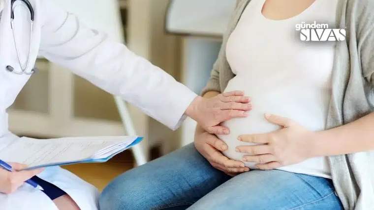 Bir doktor, hamile bir kadının karnına elini koyarak muayene ediyor.