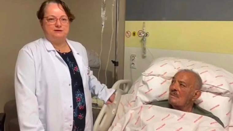 Hastane odasında bir doktor, hasta yatağında oturan bir adamın yanında duruyor.
