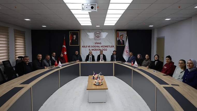 Sivas Aile ve Sosyal Hizmetler İl Müdürlüğü'nde bir toplantı odası, masanın etrafında oturan kişiler ve arka planda Türk bayrağı ile kurum logosu görünmekte.