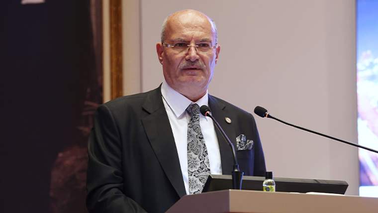 Kürsüde konuşan bir kişi, mikrofonun önünde duruyor ve izleyicilere hitap ediyor.