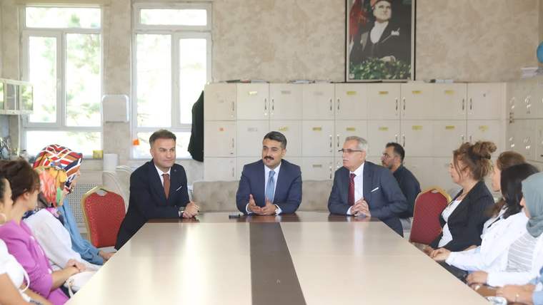 Bir sınıfta uzun masa çevresinde oturan yetişkinler ve öğrenciler karşılıklı sohbet ediyor.