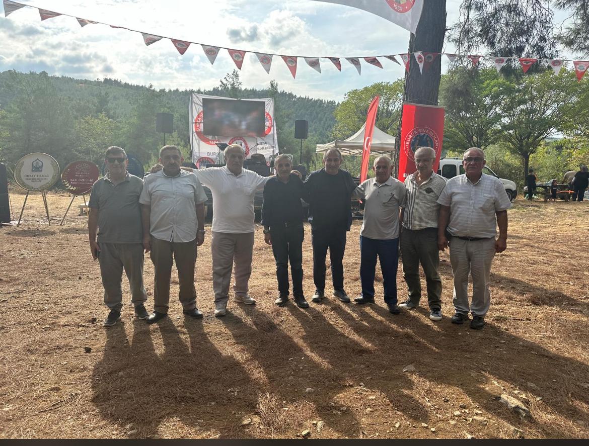 Bir grup erkek, açık alanda bir etkinlikte yan yana duruyor.