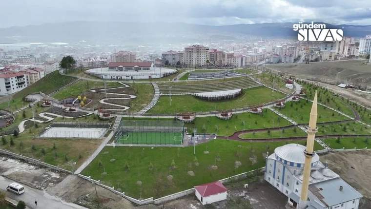 Geniş bir parkta kıvrımlı yürüyüş yolları, yeşil alanlar ve yanında minareli bir cami görülüyor.