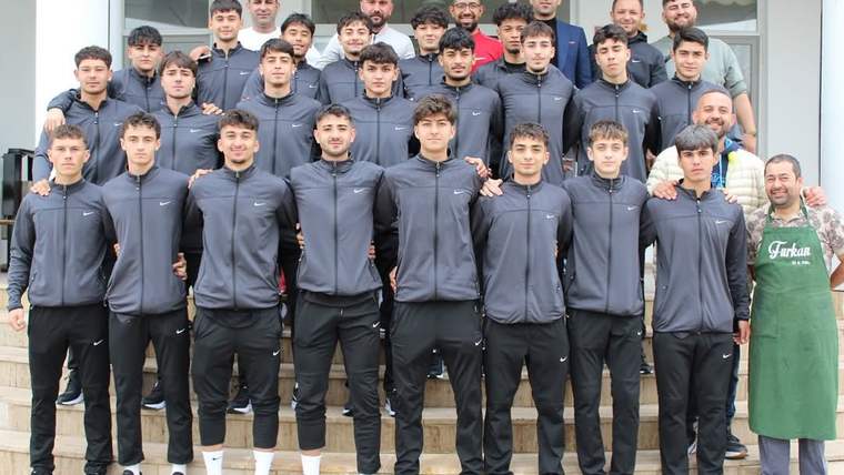 Bina girişindeki merdivenlerde, eşofmanlı bir grup genç ve yeşil önlüklü bir kişi birlikte duruyor.