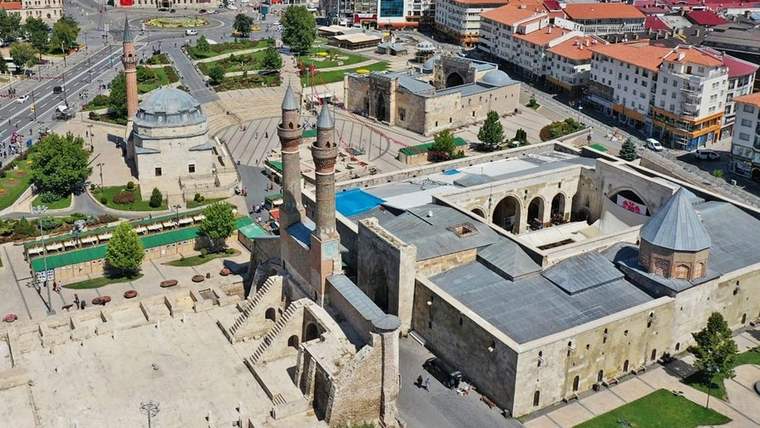Havadan görülen kent meydanında kubbeli bir cami, minare, yollar ve çevresindeki binalar yer alıyor.