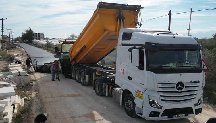 Yol kenarında damperi kaldırılmış bir kamyon, iş makineleri ve çalışanların bulunduğu alanda duruyor.