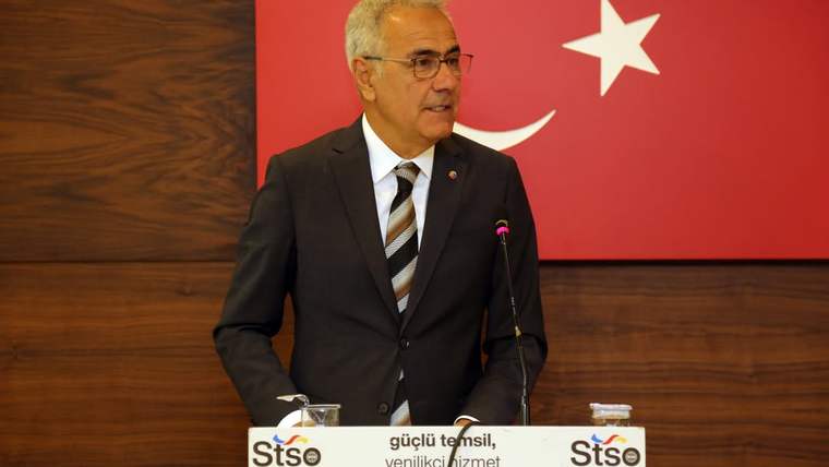 Türk bayrağı önünde kürsüde konuşan bir kişi, üzerinde STSO yazılı mikrofon ve kürsüyle görülüyor.