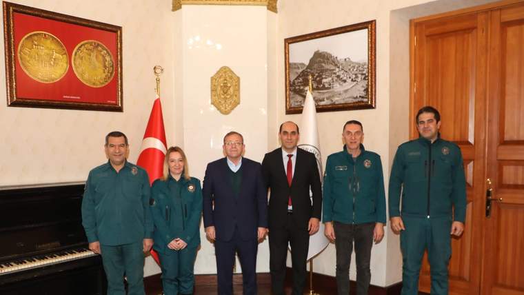 Bir odada Türk bayrağı ve başka bir bayrak önünde, beşi üniformalı altı kişi yan yana duruyor.