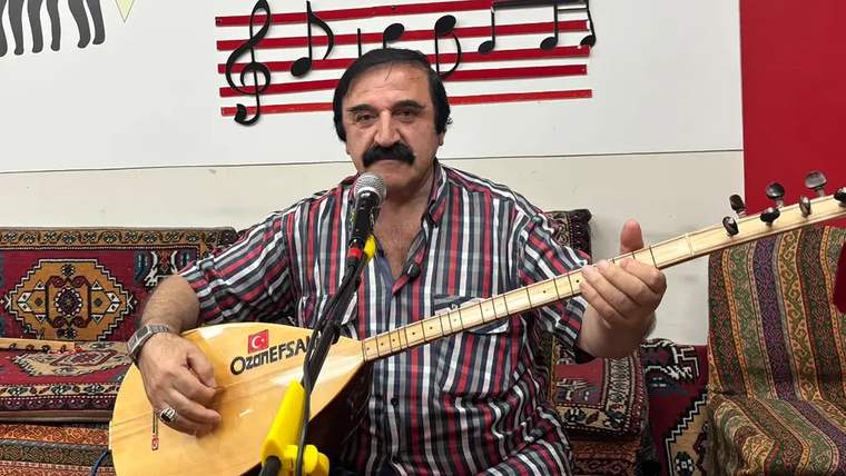 Mikrofon önünde oturan bir kişi, elinde bağlama tutuyor ve şarkı söylüyor.