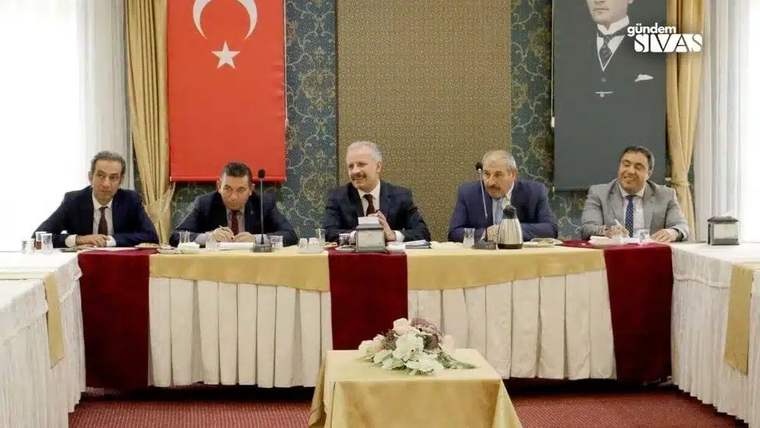 Bir toplantıda masanın etrafında oturan beş kişi, arka planda Türk bayrağı ve Atatürk posteri var.